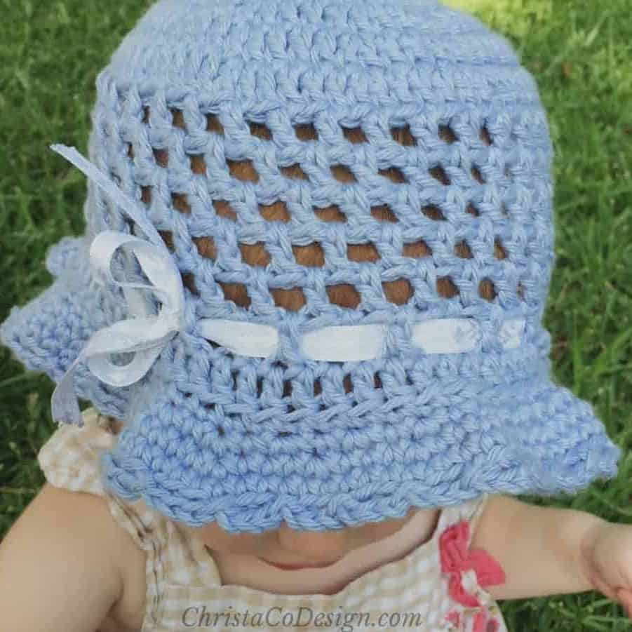 Toddler in blue sun hat with ribbon.