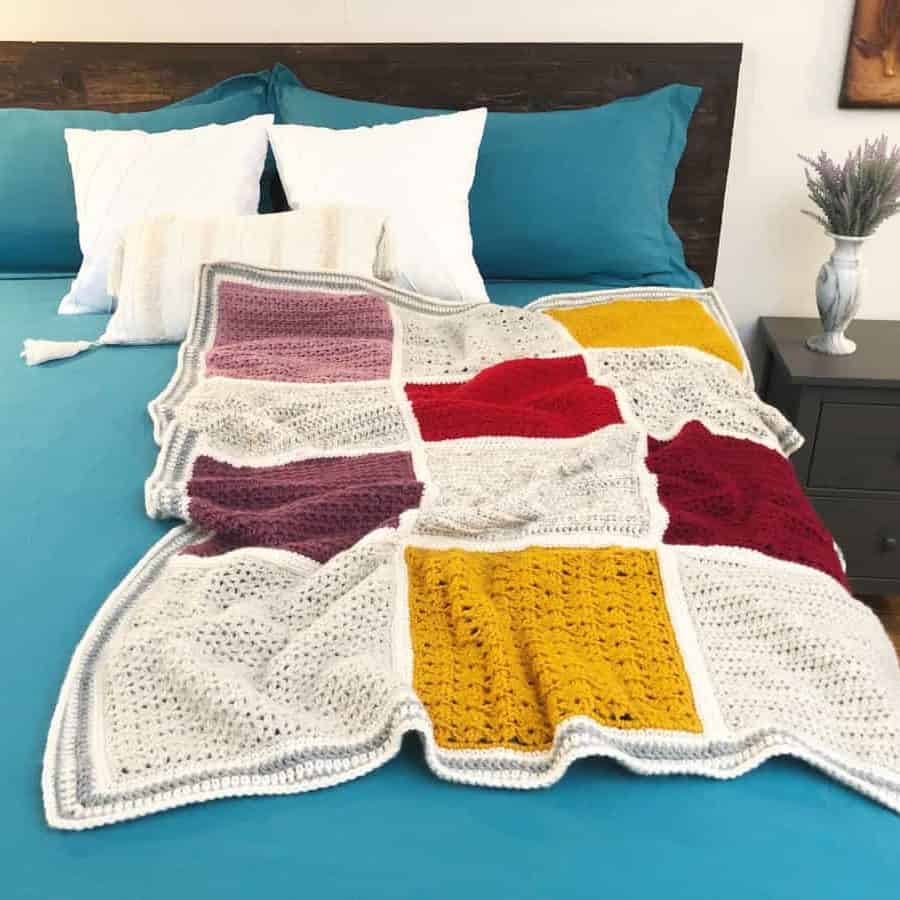 Colorful crochet blanket of squares laid on blue bedcover.