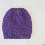 Purple knit beanie laid flat.