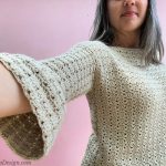 Woman in crochet sweater with arm extended showing bell sleeves.