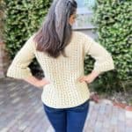 Back view of woman with hands on hips in crochet sweater with bell sleeves.