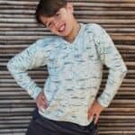 Boy in knit sweater with blue speckle with hands on hips, smiling.