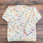 Knit v-neck sweater for kids in white with colorful speckles laid flat on wood backdrop.