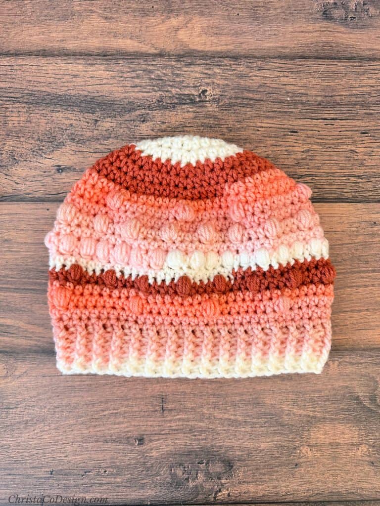 Crochet beanie with puff like texture in pink and white striped yarn.