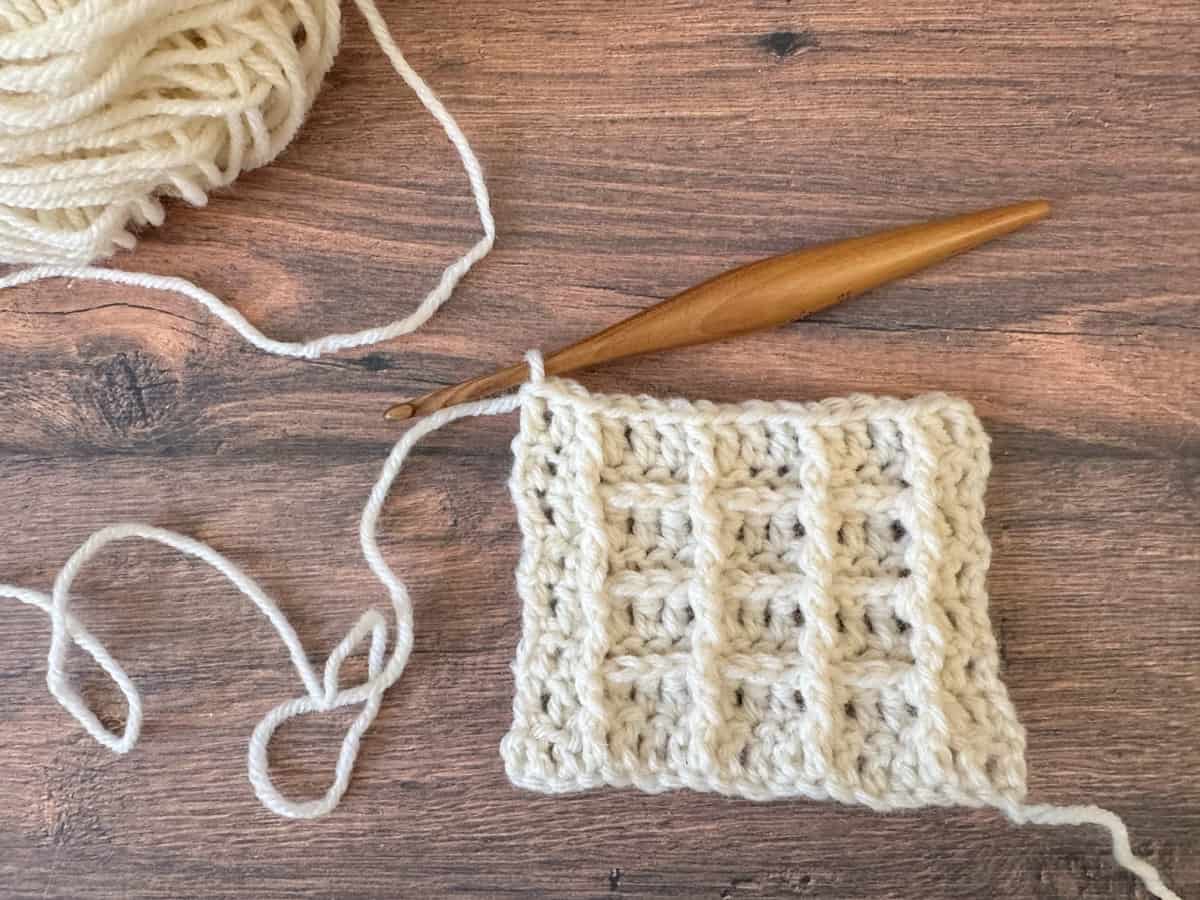 Waffle stitch square with hook and white ball of yarn.