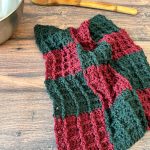 Crochet dishcloth in red and green plaid next to bowl and spoon.