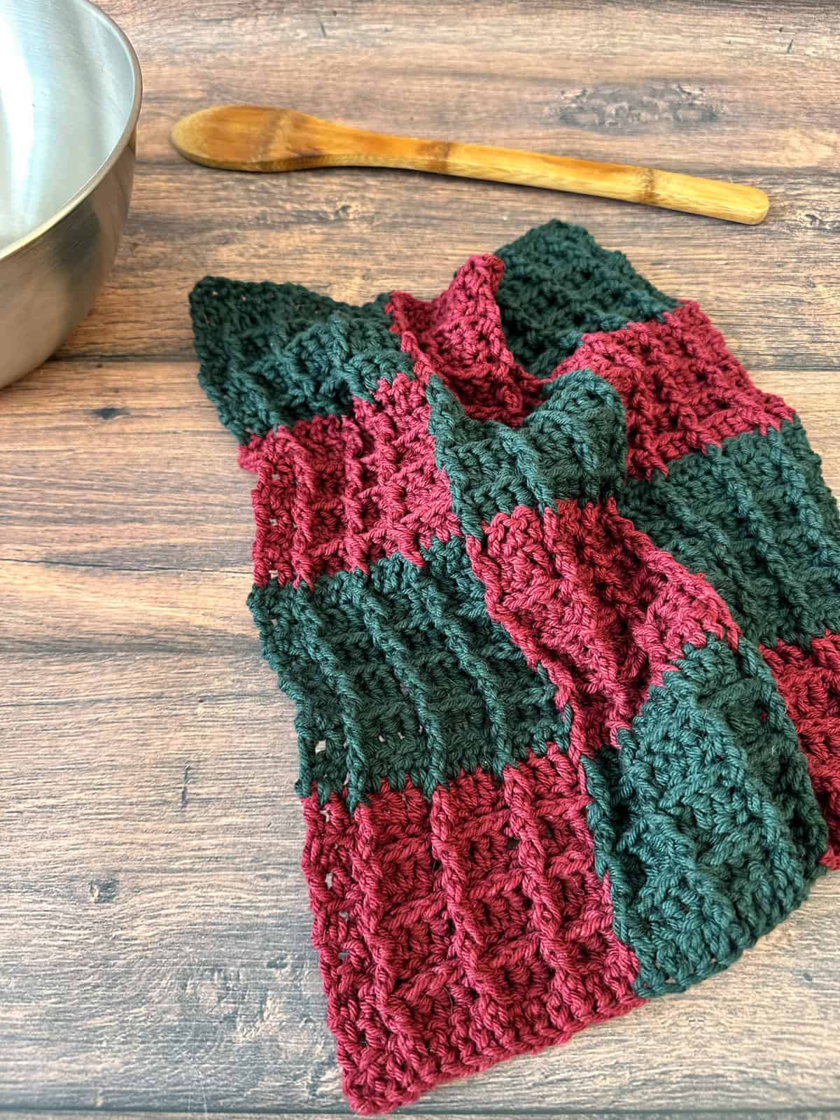 Crochet dishcloth in red and green plaid next to bowl and spoon.