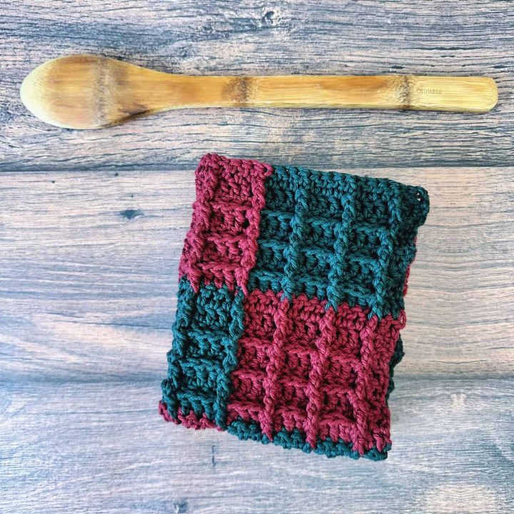 Red and green crochet dishcloth folded into square next to wood cooking spoon.