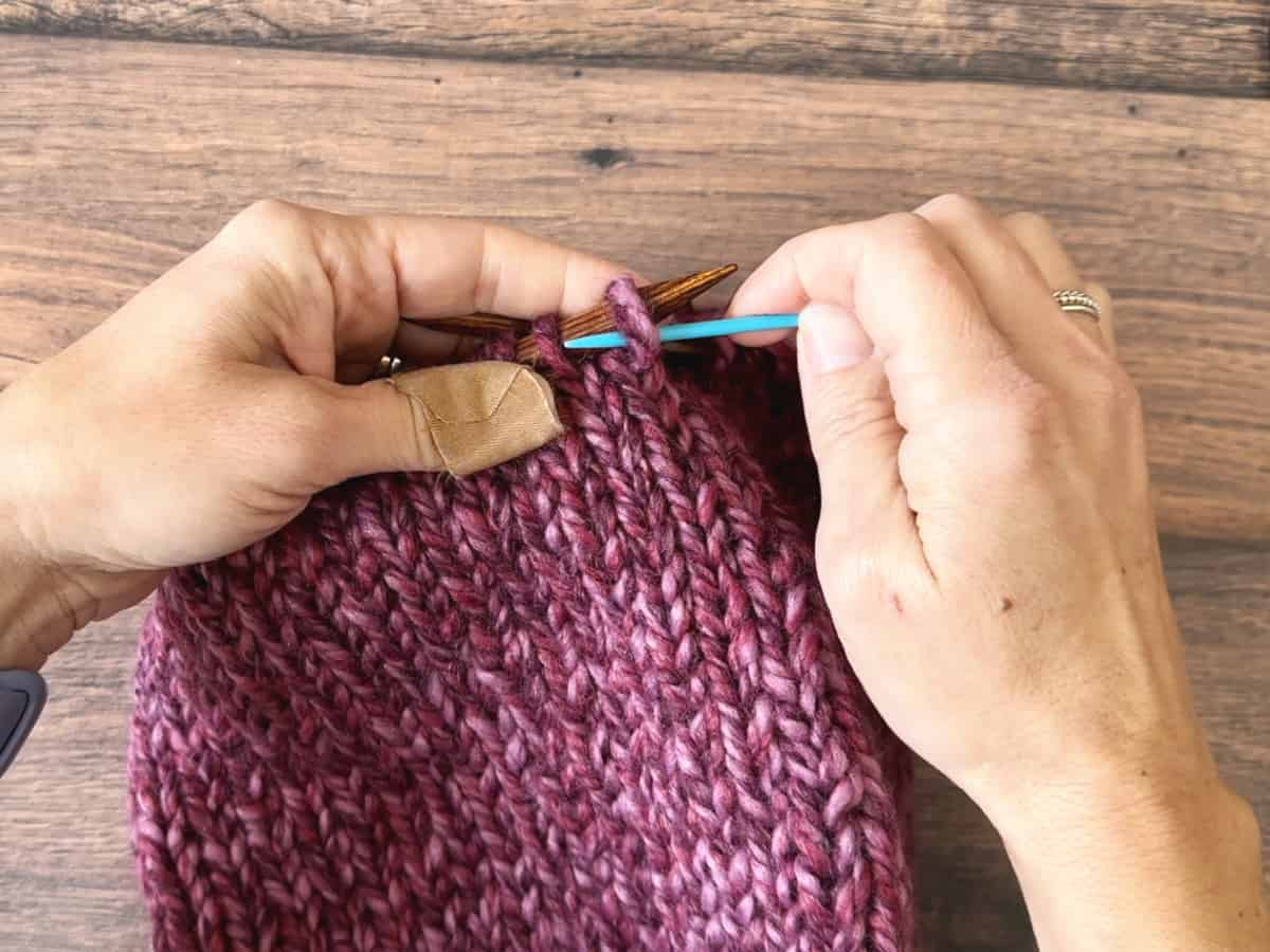 Blue yarn needle sliding stitch off.