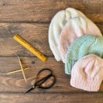 4 knit hats in white, pink and blue next to knitting notions.