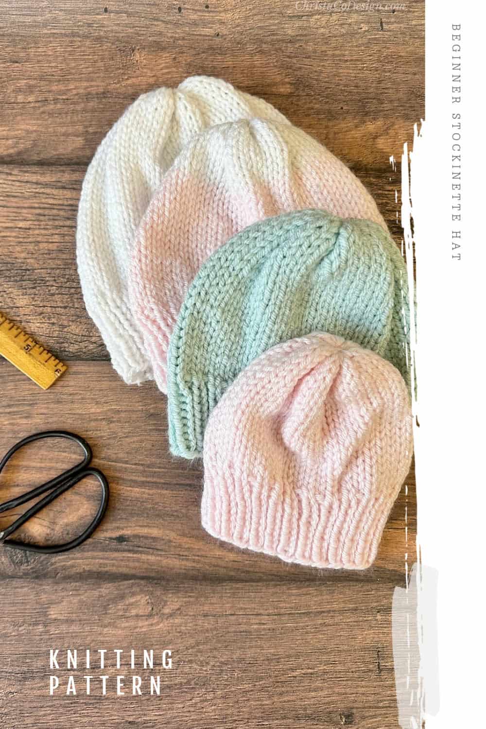 Pin image Four baby hats in white, pink and blue stacked with knitting notions.
