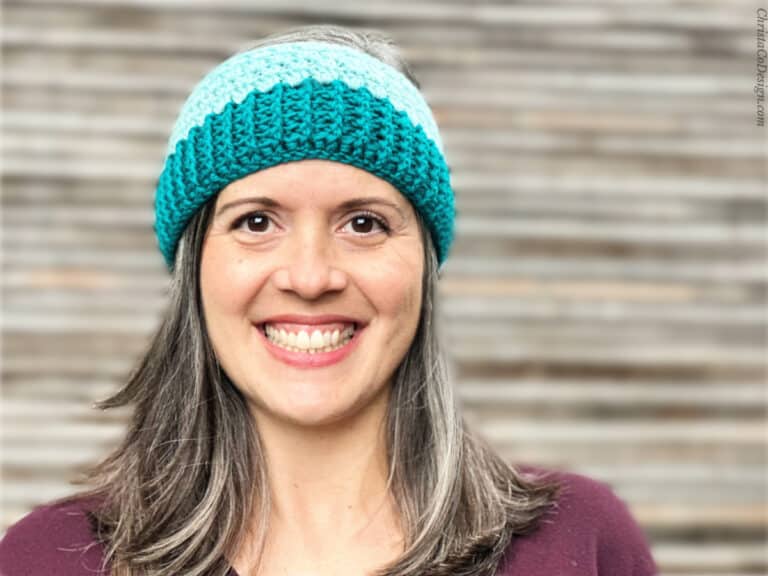 Woman wearing teal and blue crochet ear warmer smelling at camera.