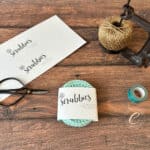 Mint crochet scrubbies wrapped in paper label surrounded by notions.