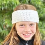 Red hair girl in white crochet earwarmer smiling at camera.