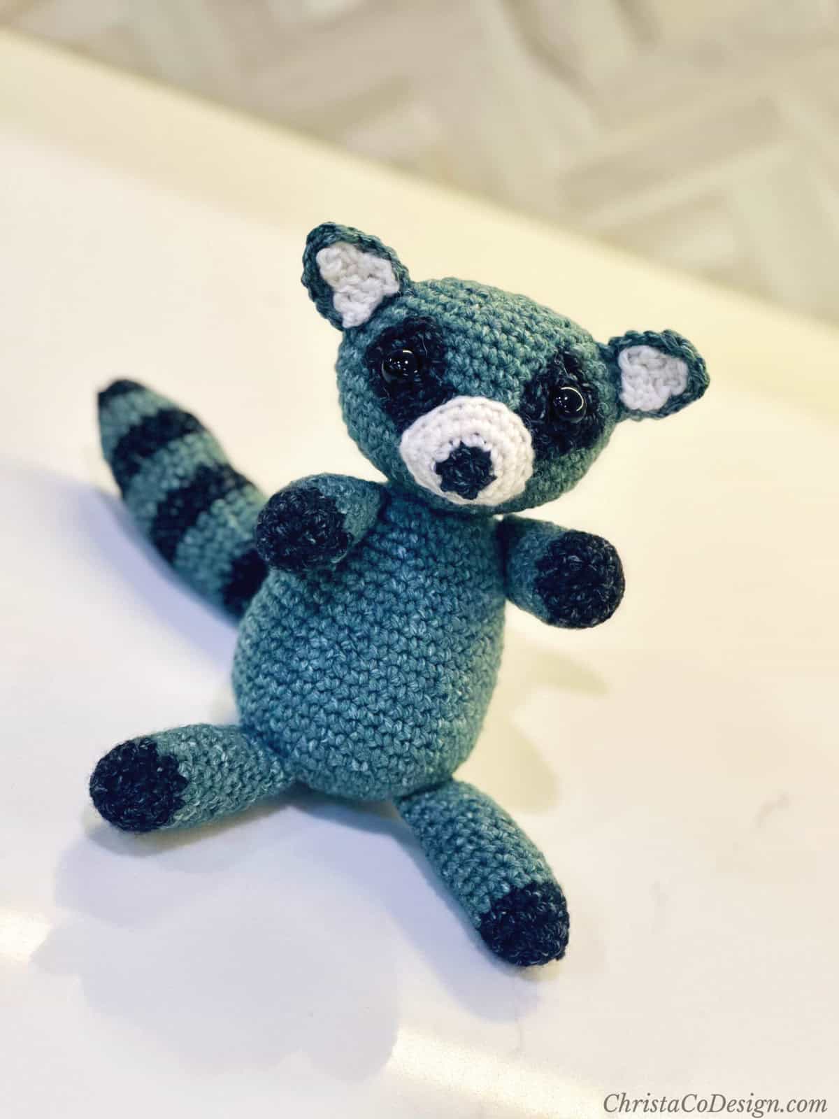 Crochet raccoon amigurumi sitting on white table.