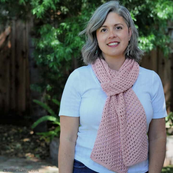 Woman outside with pink knit scarf over white shirt.