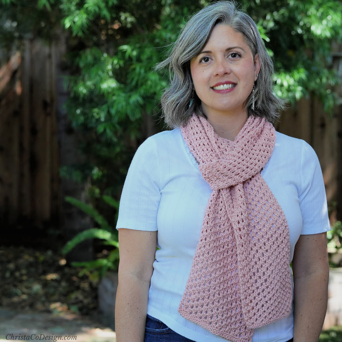 Woman outside with pink knit scarf over white shirt.