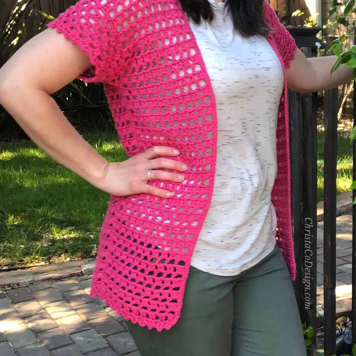 Pink open lace crochet cardigan on woman outside.
