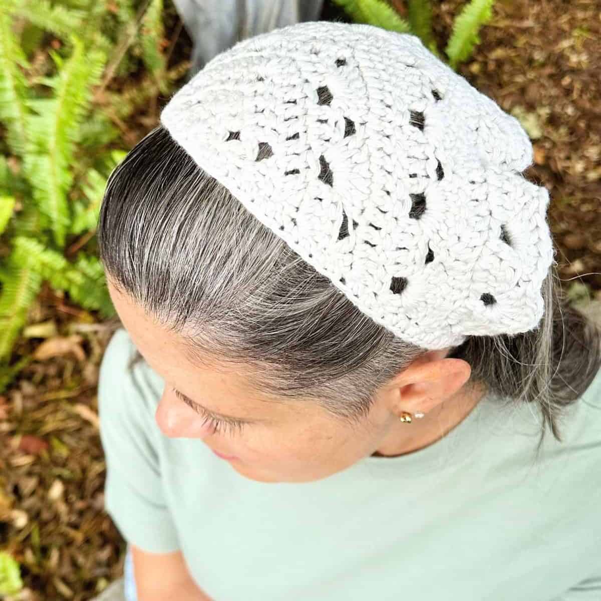 Woman sitting with pale green shirt and white bandana holding back salt and pepper hair.
