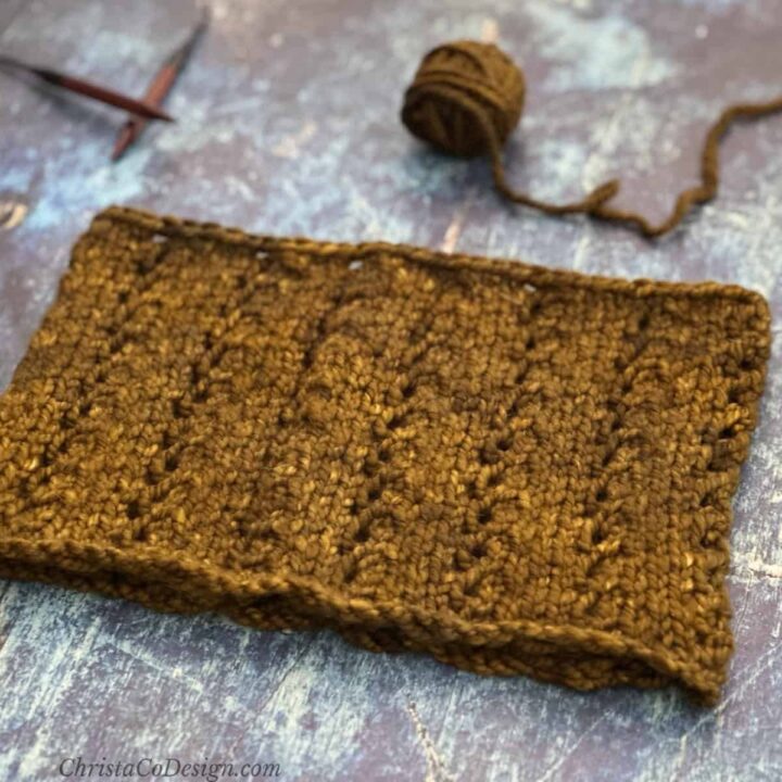 Knit cowl laid flat with needles and yarn ball.