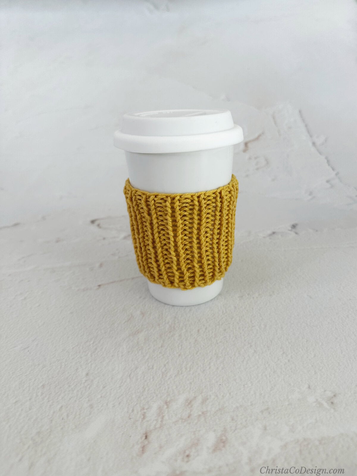 White coffee travel cup with yellow knit ribbed cozy.