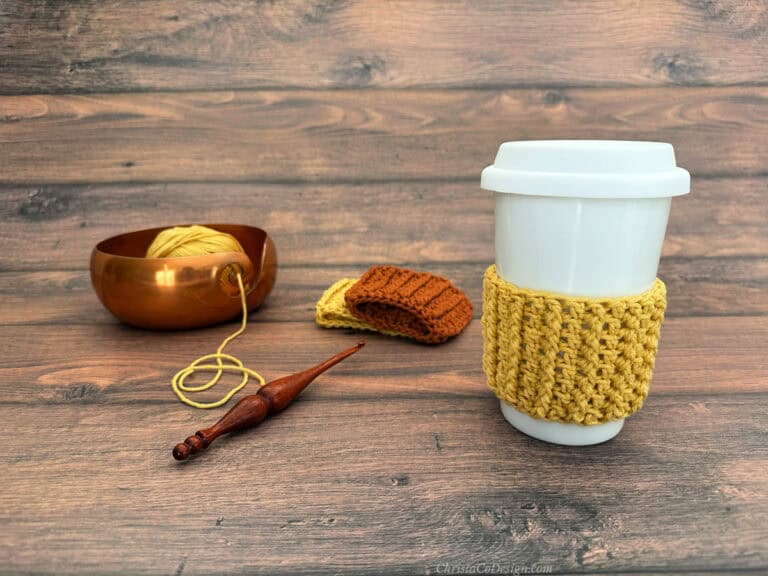 Yellow crochet cozy on white cup with yarn and notions.