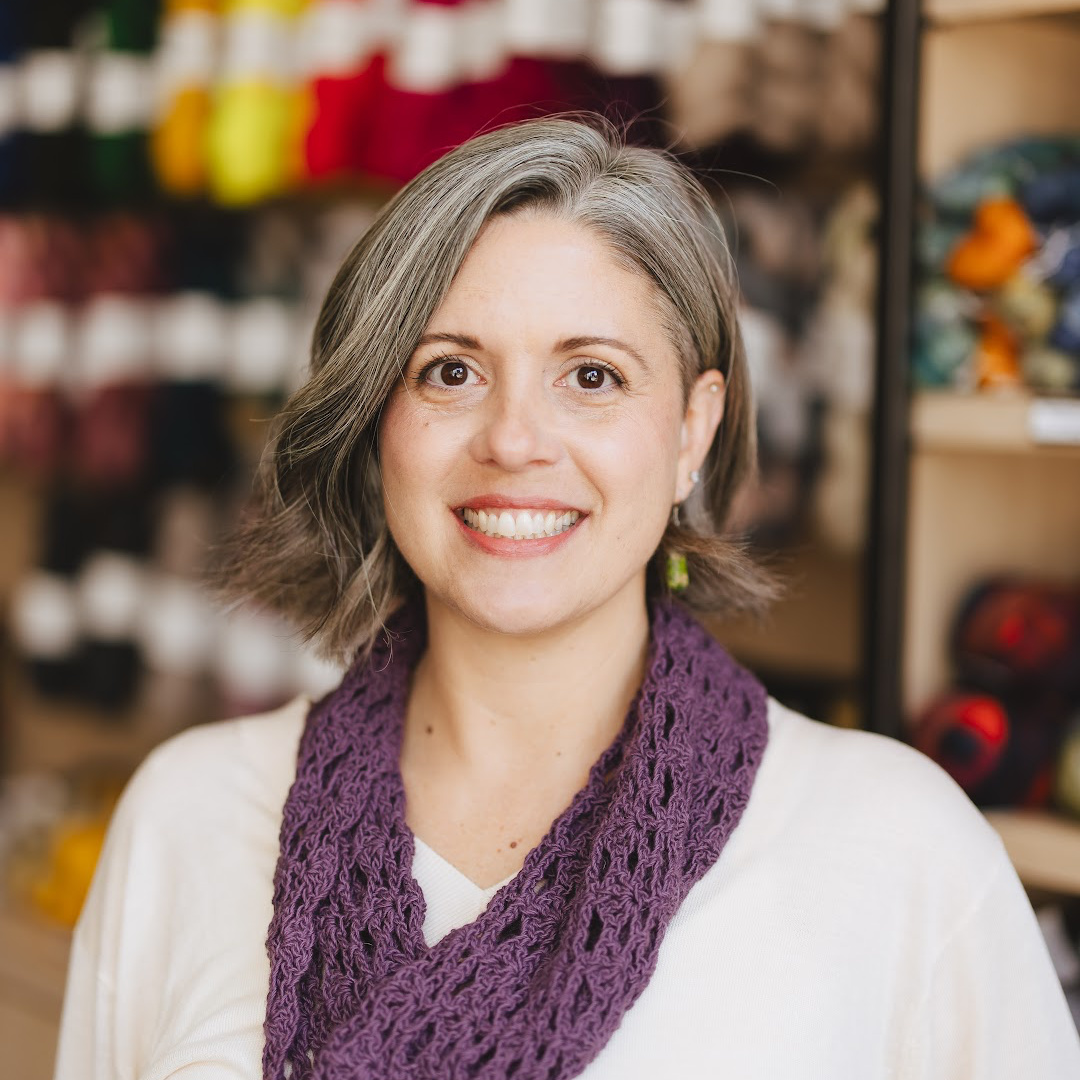 Woman smiling in front of wall of yarn.