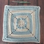 12 inch blue and white blanket square with crochet hook.