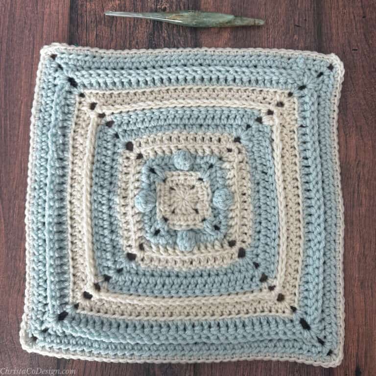 12 inch blue and white blanket square with crochet hook.