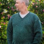 Man in green knit v-neck sweater with head turned.