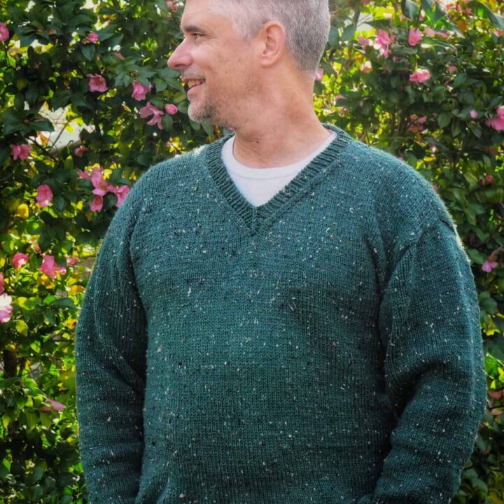 Man in green knit v-neck sweater with head turned.