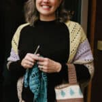 Woman smiling with crochet bag on arm with hook and shawl.