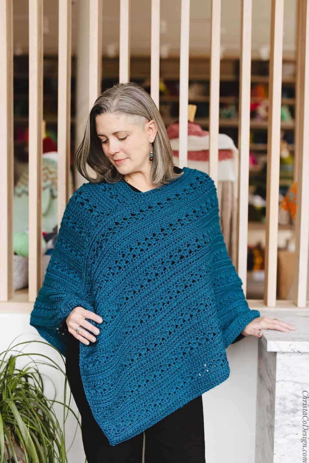 Woman looking down at crochet poncho in hand.