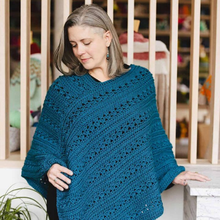 Woman looking down at crochet poncho in hand.