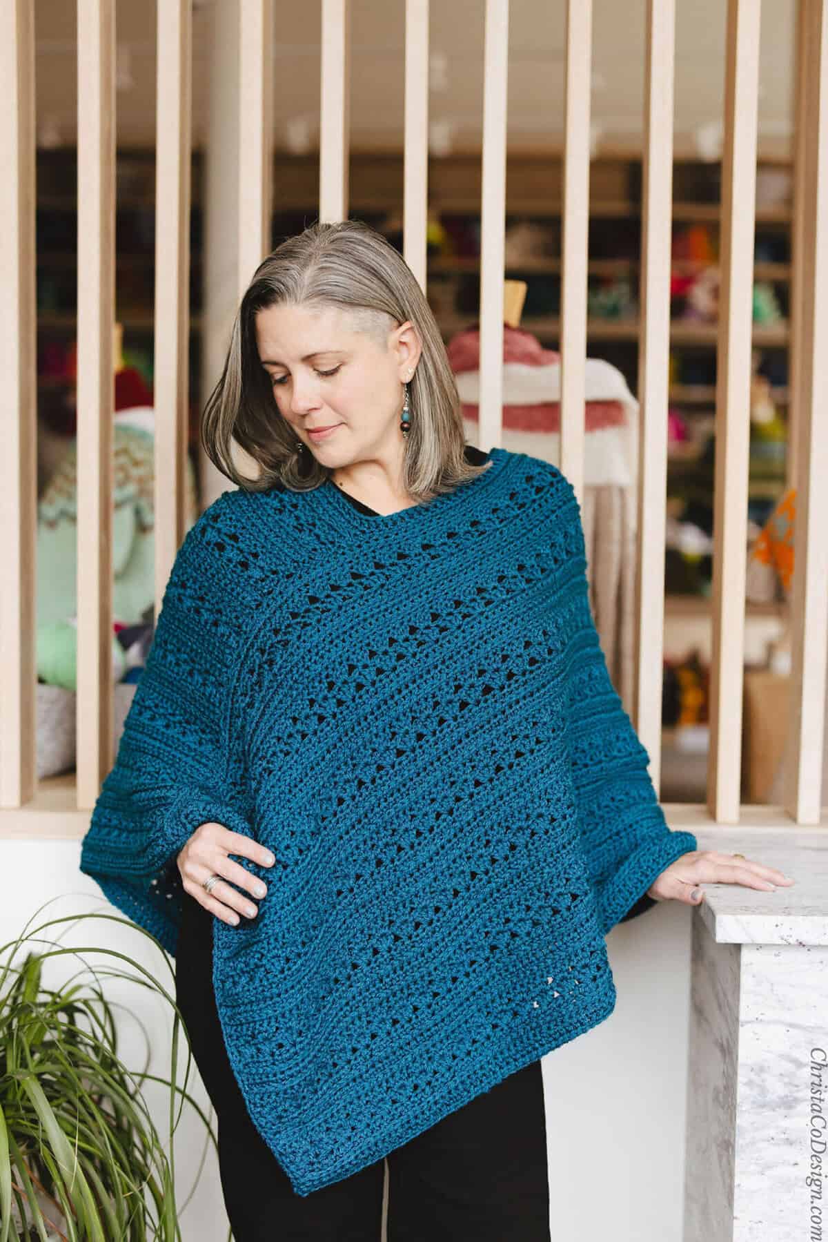 Woman looking down at crochet poncho in hand.