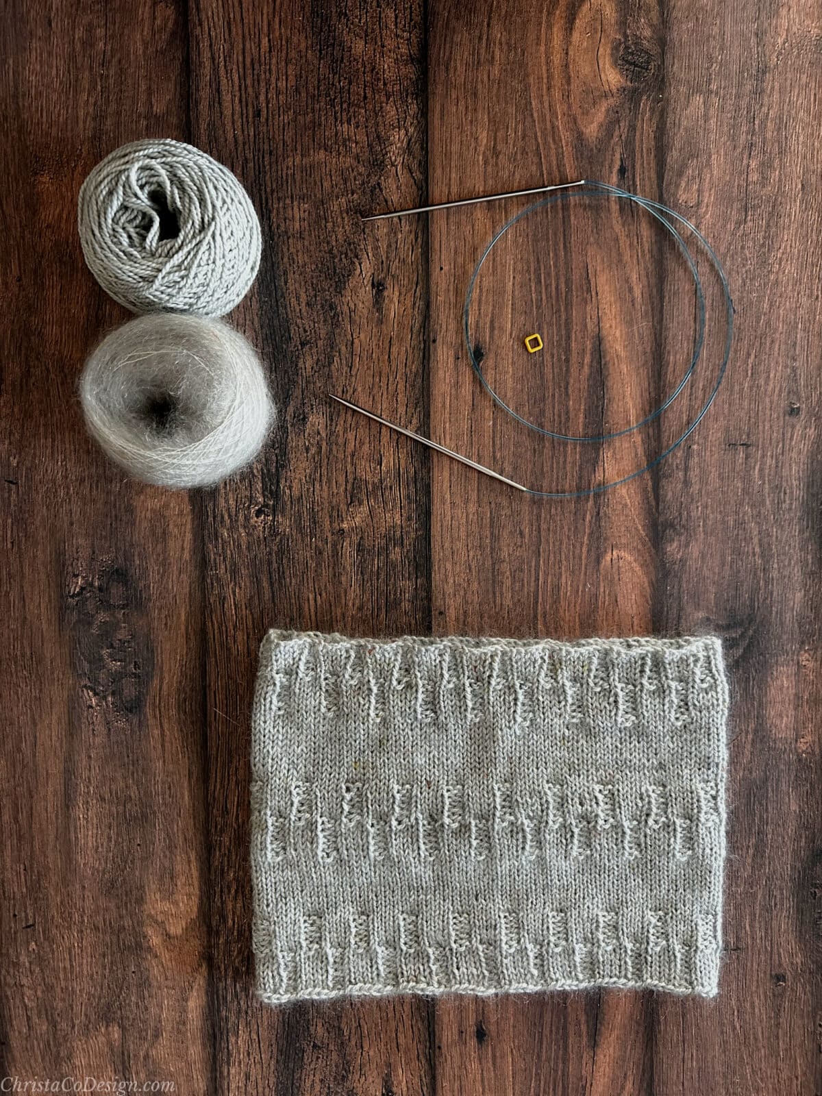 Flat lay of cowl, yarn and knitting notions.