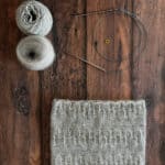 Flat lay of cowl, yarn and knitting notions.
