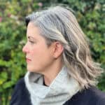Woman with head turned wearing grey cowl.