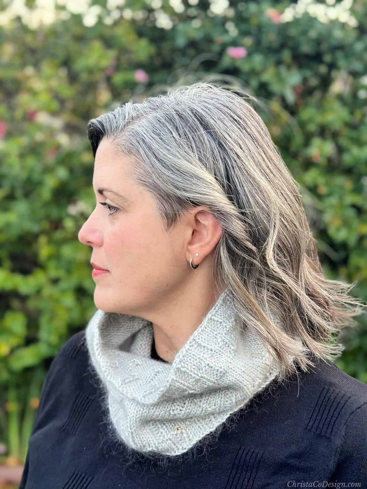 Woman with head turned wearing grey cowl.