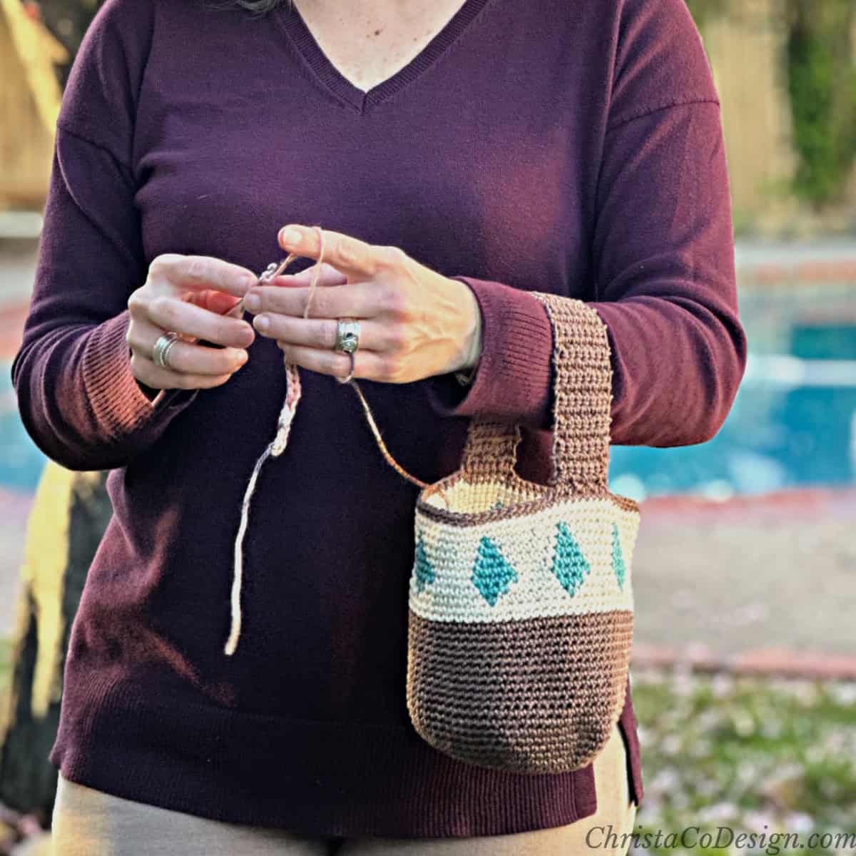 Woman with crochet bag on arm with hook and yarn.