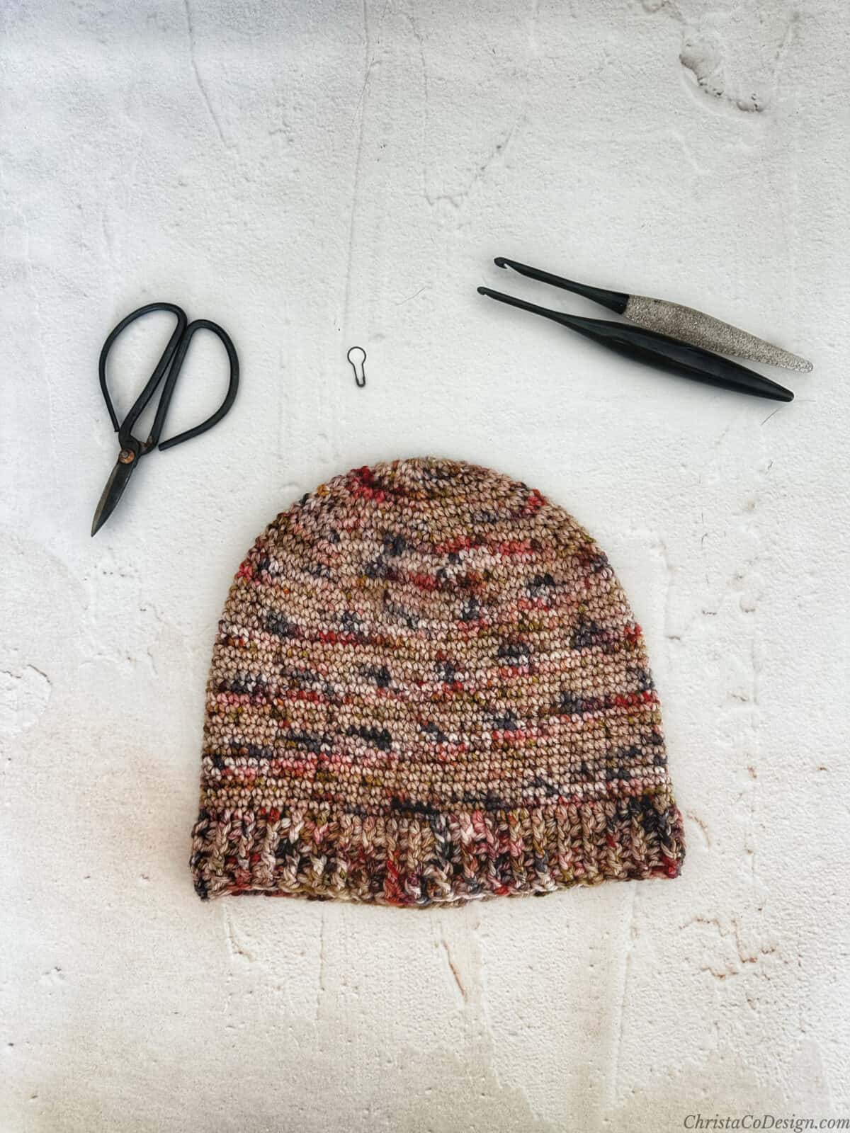 Crochet hat in variegated yarn with hooks and scissors.