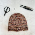Crochet hat in variegated yarn with hooks and scissors.