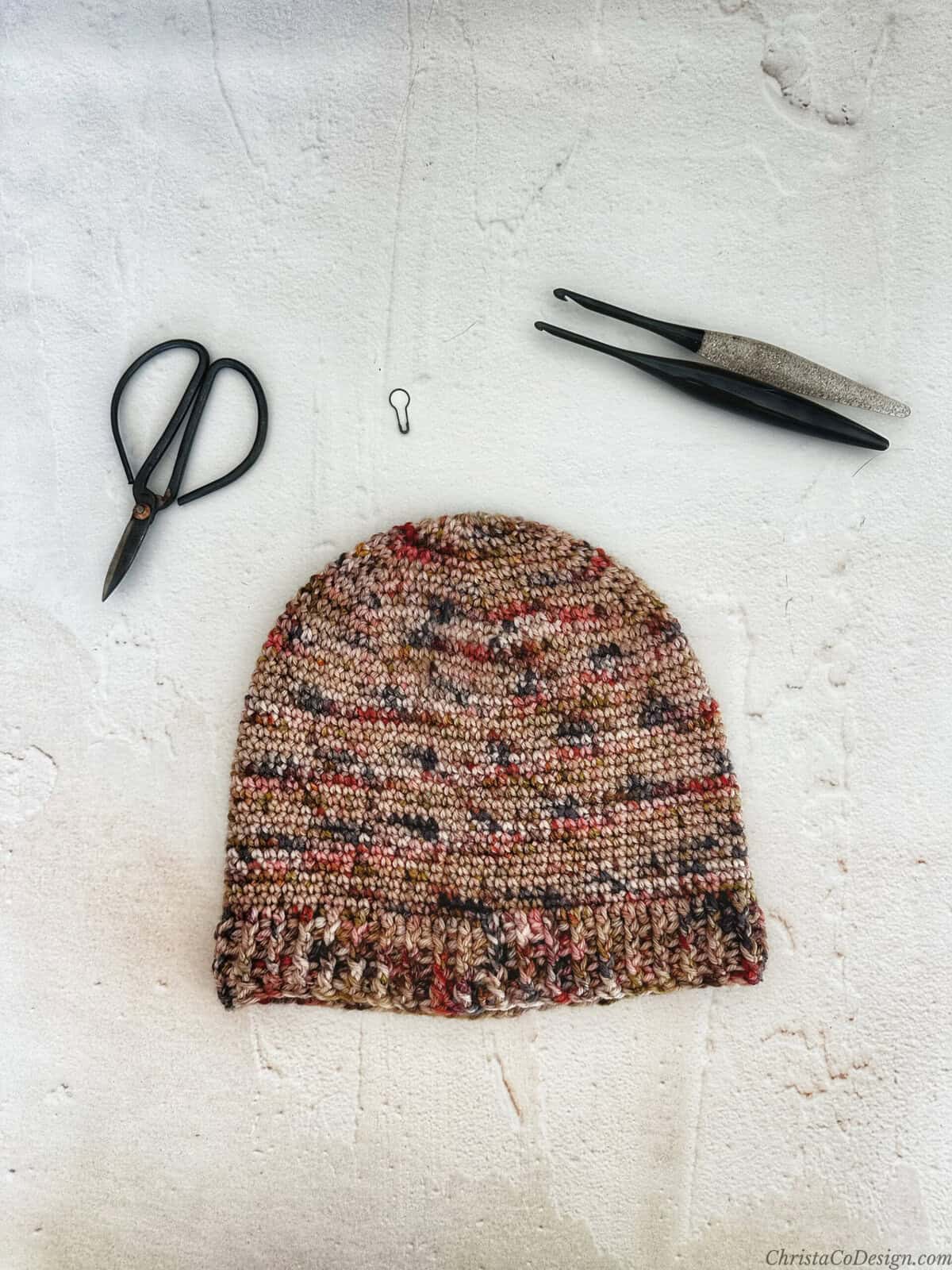 Crochet hat in variegated yarn with hooks and scissors.