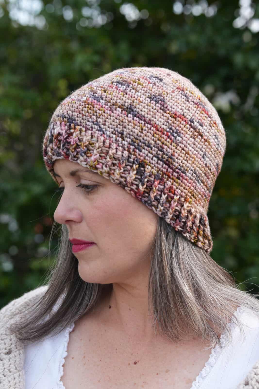 Woman smiling with crochet hat in shades of pink and browns.