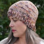 Woman smiling with crochet hat in shades of pink and browns.