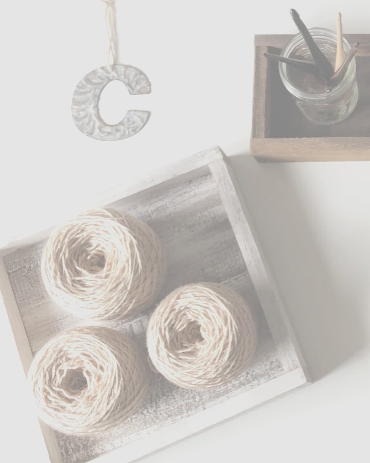 Flat lay 3 yarn cakes on wood square next to C and hooks.