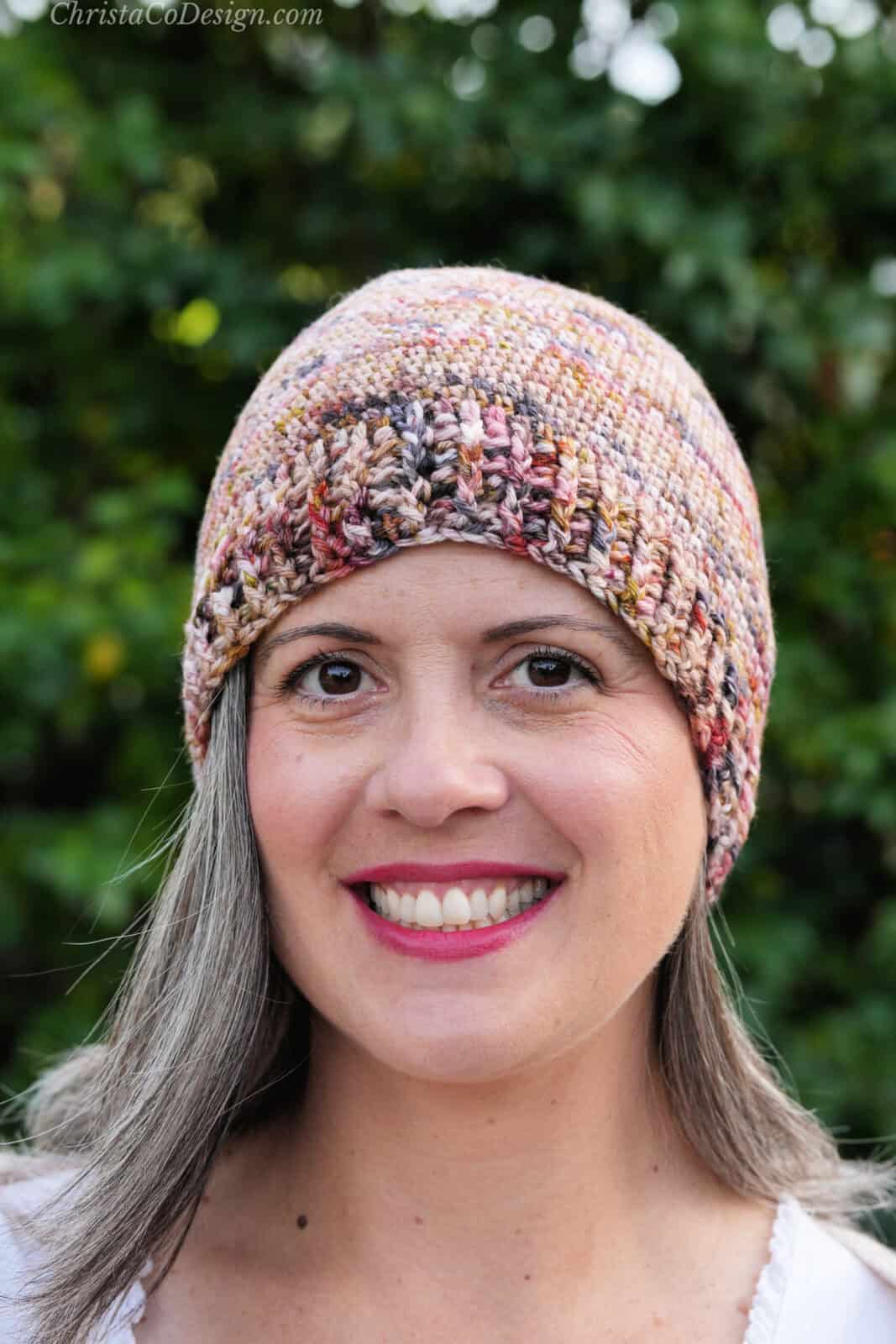 Woman smiling with crochet hat in shades of pink and browns.