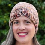 Woman smiling with crochet hat in shades of pink and browns.