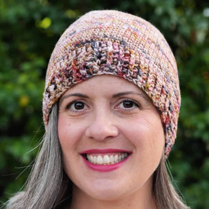 Woman smiling with crochet hat in shades of pink and browns.