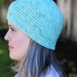 Woman in blue crochet hat turned to side.
